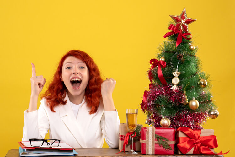 圣诞树女工人坐在桌子后面 手里拿着圣诞礼物和黄色的圣诞树圣诞节整理桌子
