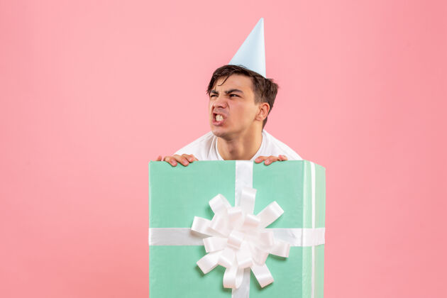 快乐一个年轻人躲在粉红色的墙上礼物的正面视图礼物盒子圣诞快乐