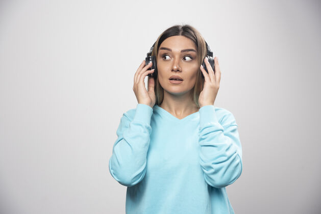 女人穿着蓝色运动衫的金发女孩戴着耳机 努力听懂音乐Dj耳机音乐