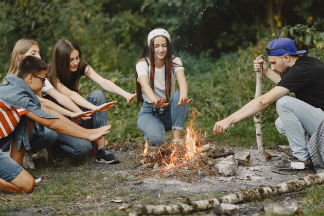 生态探险 旅游 远足和人的概念一群微笑的朋友在森林里人们坐在篝火旁旅游火森林