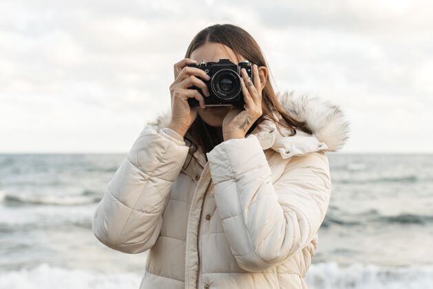冬天夹克海滩上带着相机的女人的正视图旅行水平独自