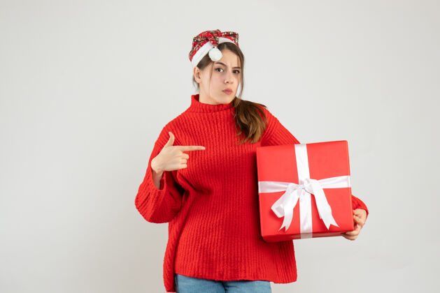 可爱带着圣诞帽的怀疑女孩拿着礼物用手指着盒子白色的东西圣诞节怀疑帽子