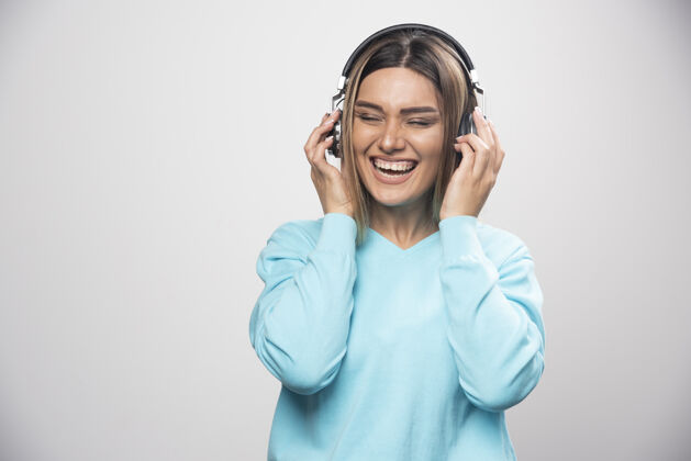 耳机穿着蓝色运动衫的金发女孩戴着耳机 享受着音乐和乐趣年轻乐趣Dj
