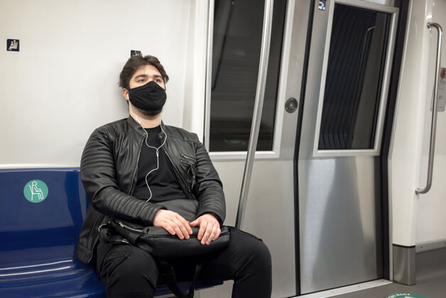 面罩一个留着胡子戴着耳机戴着黑色医用口罩的白种人坐在地铁的椅子上地铁医疗面罩