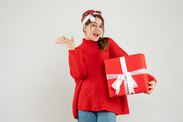 圣诞老人戴着圣诞帽的快乐女孩拿着礼物盒站在白色的地板上礼物快乐圣诞节