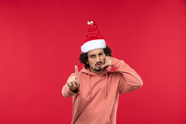 圣诞节红墙上年轻人模仿电话的正面图人帽子男人