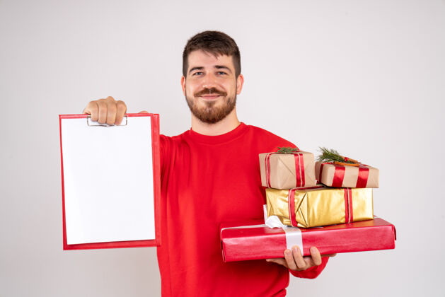 人们身穿红衫的年轻人拿着圣诞礼物和白墙上的文件说明的正面视图举行节日微笑