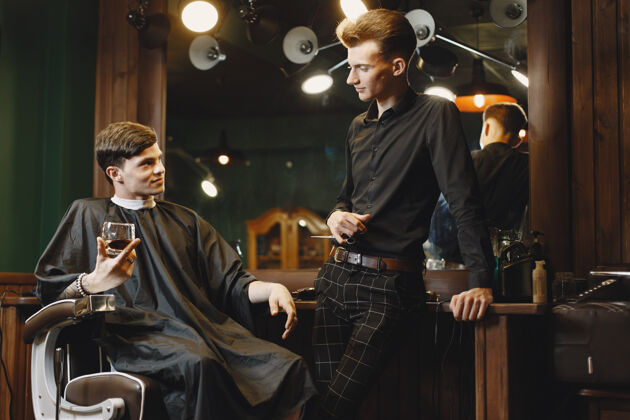 胡须坐在椅子上的男人和客户在一起的理发师喝威士忌的家伙时尚小胡子头