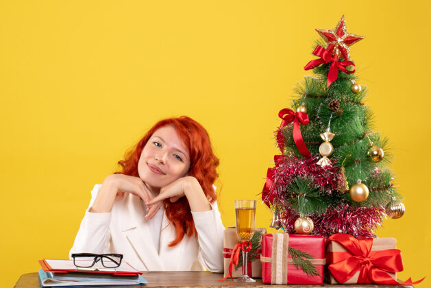 情感前视图：女医生坐在桌子后面 黄色背景上有圣诞礼物女医生人女性