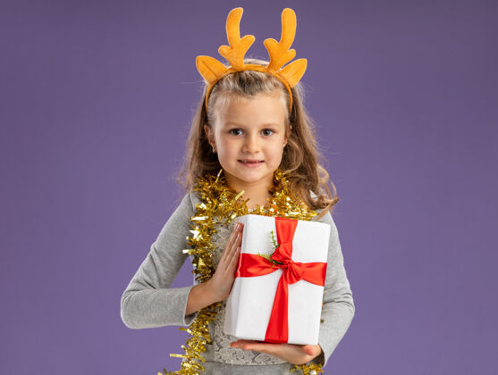 抱着高兴的小女孩戴着圣诞发箍 脖子上戴着花环 手里拿着蓝色背景的礼品盒女孩圣诞快乐快乐