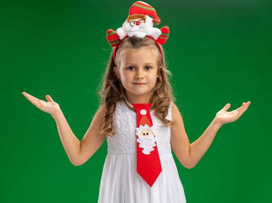 头发可爱的小女孩戴着圣诞发箍 打着领带 双手分开放在绿色的背景上小圣诞节高兴