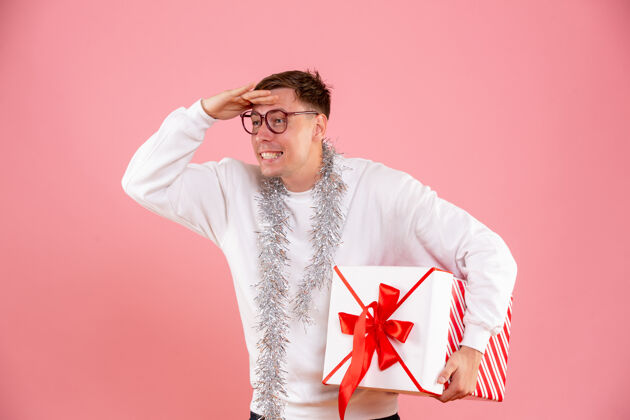 快乐一个年轻人拿着圣诞礼物在粉红色的墙上遥望远方人盒子人