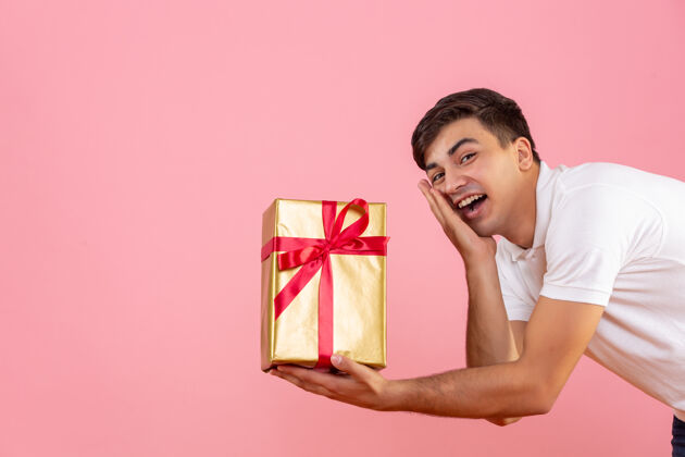 赠送在粉红色的墙上年轻人给某人送圣诞礼物的正面图快乐正面十二月