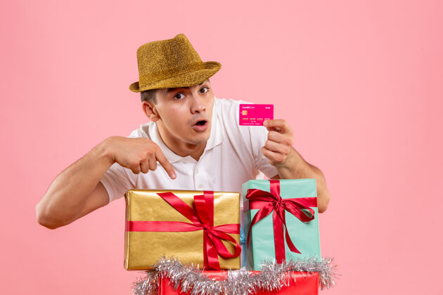 微笑年轻人在圣诞节前的照片 粉红色的墙上挂着一张银行卡帽子人快乐