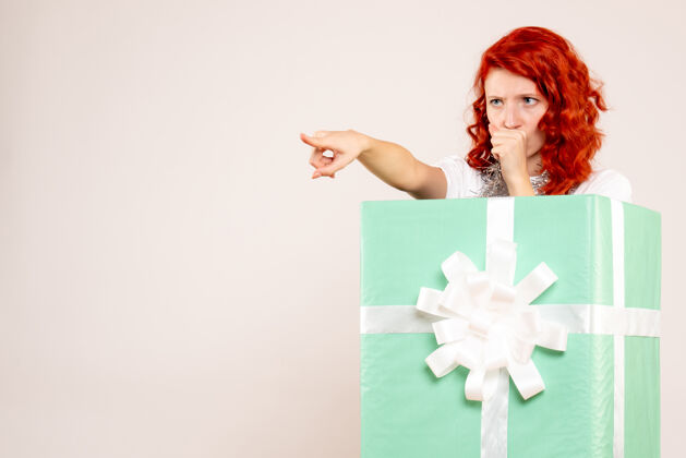 节日一个年轻女子躲在一个白色的墙内礼物的正面视图隐藏圣诞节庆祝