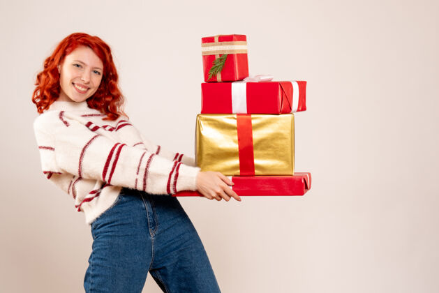 十二月前视图的年轻女子携带圣诞礼物的白墙礼物圣诞快乐女性