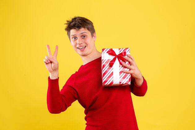 举行黄色墙上年轻人拿着圣诞礼物的正面图微笑情感十二月