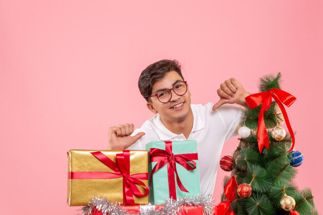 年轻圣诞礼物和粉红色墙上的圣诞树周围的年轻人的正面视图成人礼物圣诞