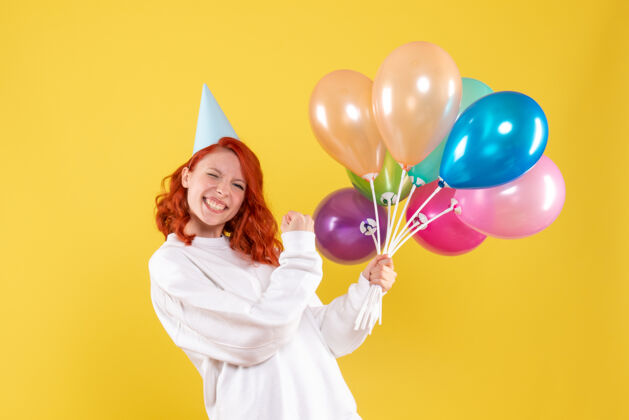 丝带黄色墙壁上手持彩色气球的年轻女子的正视图生日乐趣年轻