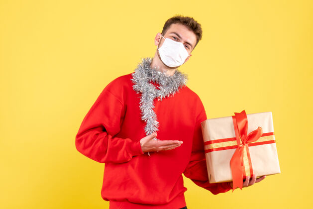 圣诞节正面图：戴着无菌面具的年轻男性手持圣诞礼物脸流行性年