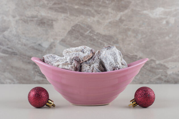 水果一碗涂有糖粉的干柿子放在大理石背景上的圣诞饰品旁边粉碗干的