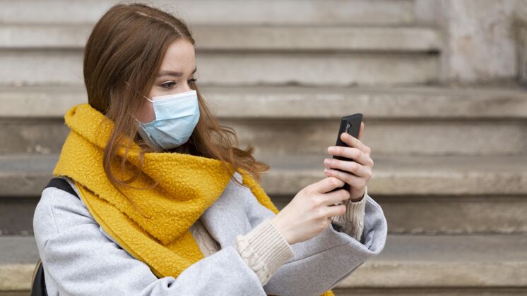 安全戴着医用口罩的女人用智能手机拍照智能手机水平面罩