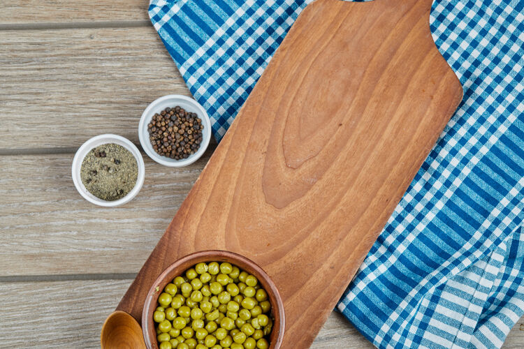 有机的木桌上放着一碗煮青豌豆 调味品和一块蓝色桌布滋补全蒸熟