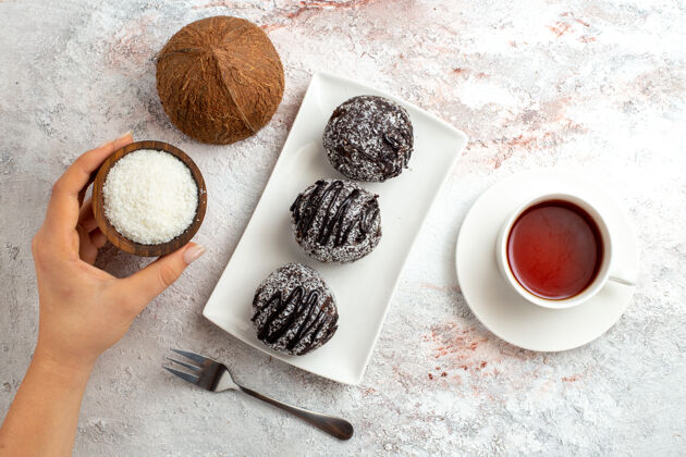 椰子俯瞰巧克力蛋糕与一杯茶和椰子的白色表面巧克力蛋糕饼干糖甜饼干脸粉化妆品生