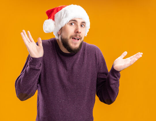 圣诞老人一个穿着紫色毛衣 戴着圣诞帽的年轻人站在橙色的背景下 困惑地耸耸肩 看不到回答肩膀困惑耸肩