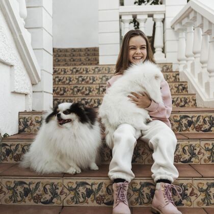 同伴女孩和可爱的白色小狗坐在楼梯上快乐孩子可爱