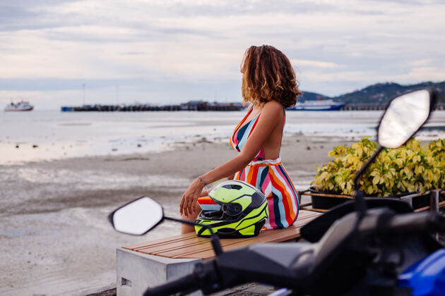 旅游快乐的高加索骑摩托车的女人 穿着五颜六色的夏装 戴着摩托车头盔度假车辆户外交通