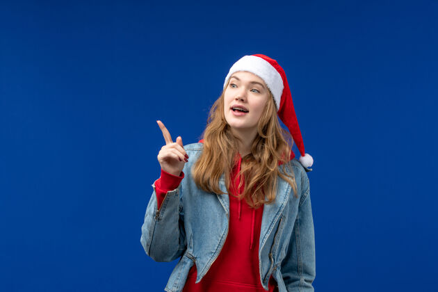 年轻女性正面图蓝色背景上戴着红色圣诞帽的年轻女性感慨圣诞假期快乐帽子人