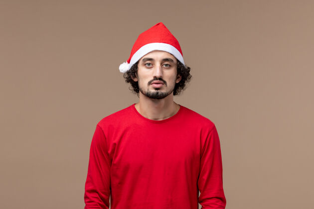 成人正面图：棕色背景上穿着红色圣诞斗篷的年轻男性情感节日圣诞节背景正面工人