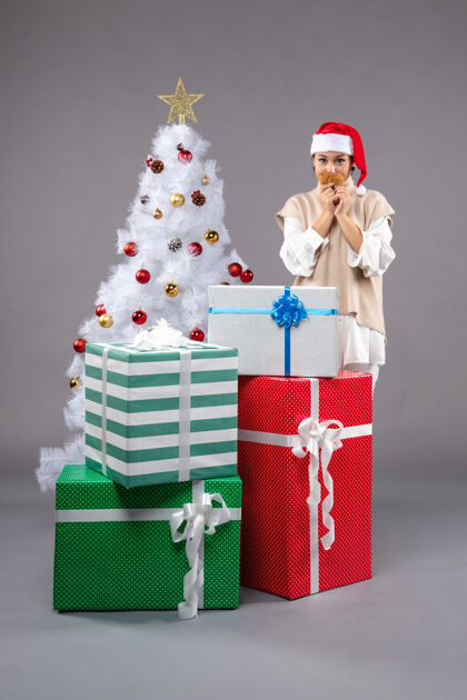 圣诞在圣诞树旁的灰色地板上 年轻的女人拿着饼干和礼物年轻女性礼物饼干