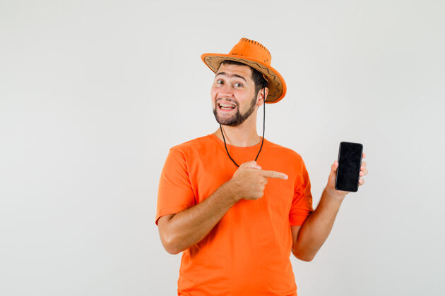 衬衫年轻人指着手机 穿着橙色t恤 戴着帽子 看上去很快乐前视图表情男人成人