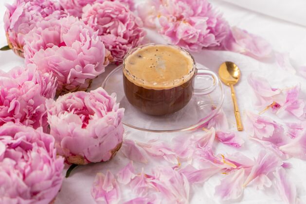 玻璃一杯速溶咖啡放在桌上的茶碟上的特写镜头 上面有粉色的牡丹花热博客咖啡