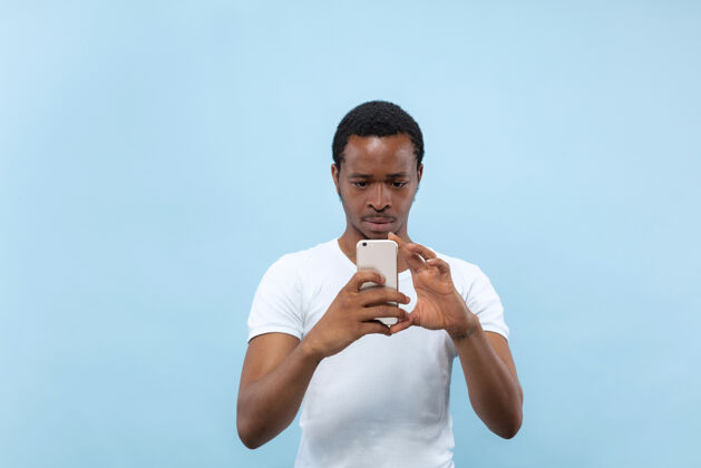 表情身穿白衬衫的非洲裔美国年轻人的特写肖像……在智能手机上拍照或录制视频博客内容观点男人虚拟博客