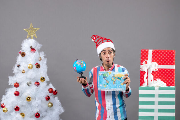 惊喜前视图惊讶的人拿着世界地图和地球仪在圣诞树和礼品盒附近假期人有趣