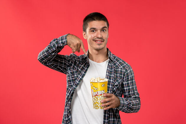 男人正面图年轻男性手持爆米花在浅红色的墙上男性电影院年轻剧院观点
