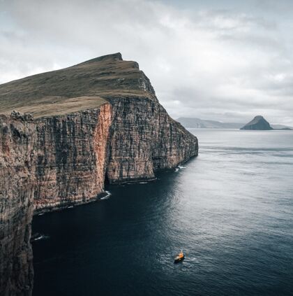 海岸拍摄捕捉美丽的自然法罗群岛 一艘船漂浮在海边的悬崖景自然海