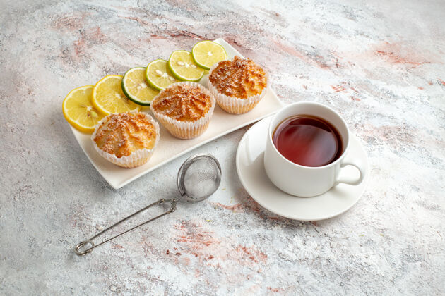 柠檬前视图小蛋糕烘烤和甜柠檬片和一杯茶的白色表面蛋糕饼干面团糖甜饼干茶杯子饼干