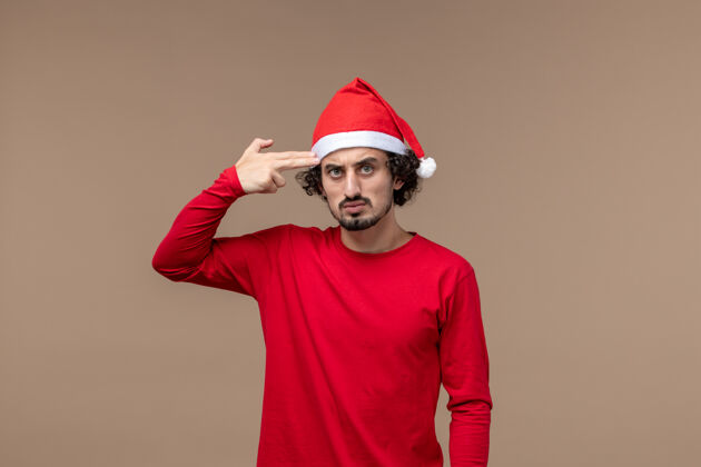 帽子正面图：在棕色背景上穿着红色圣诞斗篷的年轻男性感慨圣诞假期棕色工人工程师