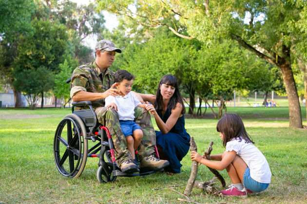 满一对沉思而平和的父母在户外和孩子们一起度过闲暇时光 在草地上布置柴火残疾退伍军人或家庭户外概念侧视图父亲日志