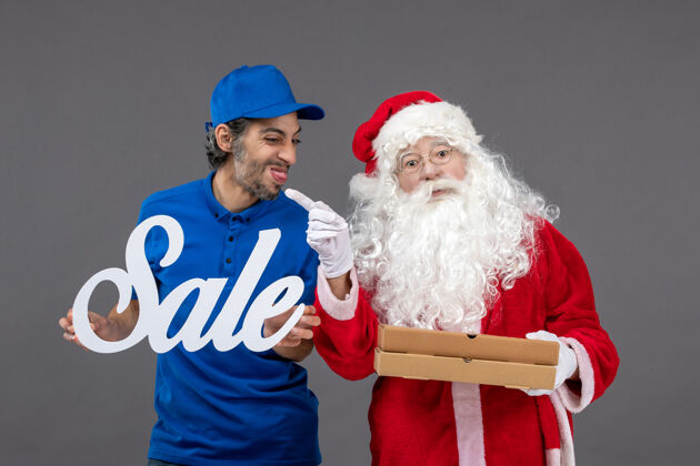 男性圣诞老人的正面图 男信使手持销售横幅 灰色墙上有食品盒男人盒子十二月