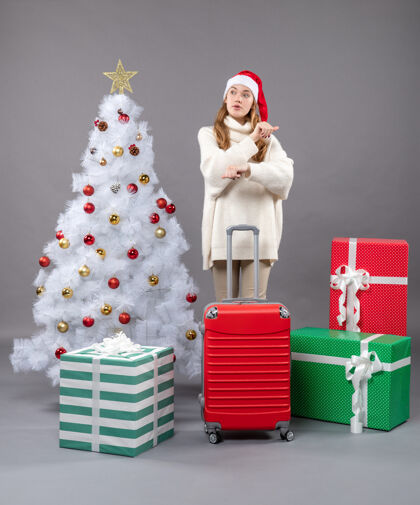 圣诞帽正面图：站在圣诞树旁的一个带着红色手提箱的惊讶女孩圣诞礼物圣诞树行李