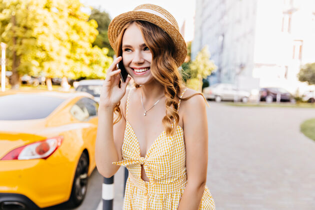 智能手机浅棕色的女模特 带着可爱的微笑在打电话热情的白人女孩穿着黄色格子裙 拿着智能手机摆姿势寒冷金发城市景观