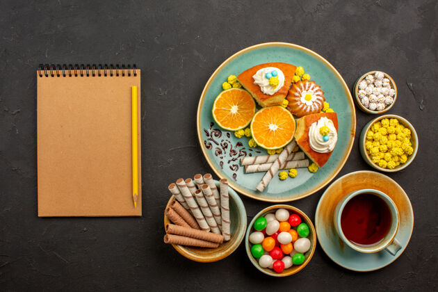 装置顶视图美味的派片与新鲜的橘子茶和糖果在黑暗中盘子餐蛋糕