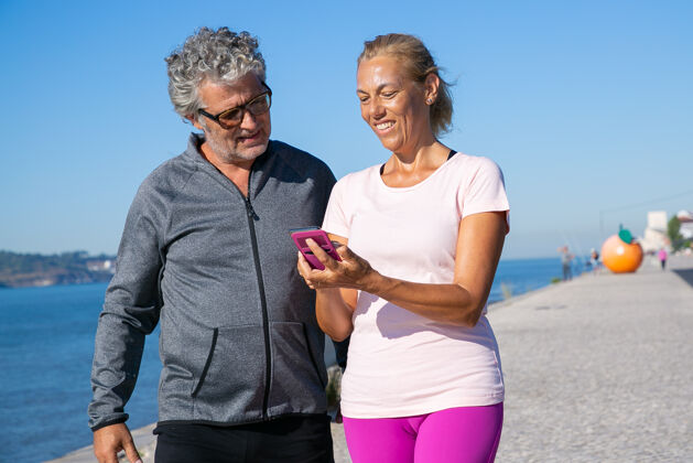 户外积极成熟的女性在慢跑后使用手机上的健身应用程序 向男性展示屏幕交流和运动概念的小工具老年人拍摄中等