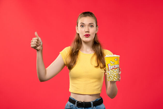 年轻女性前视图年轻女性在电影院拿着爆米花包 在红墙电影院摆姿势女性趣味电影电影电影爆米花