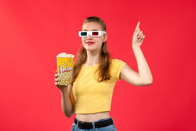 电影正面图年轻女性在电影院拿着爆米花戴着d太阳镜上红墙电影院女彩色剧院颜色女性